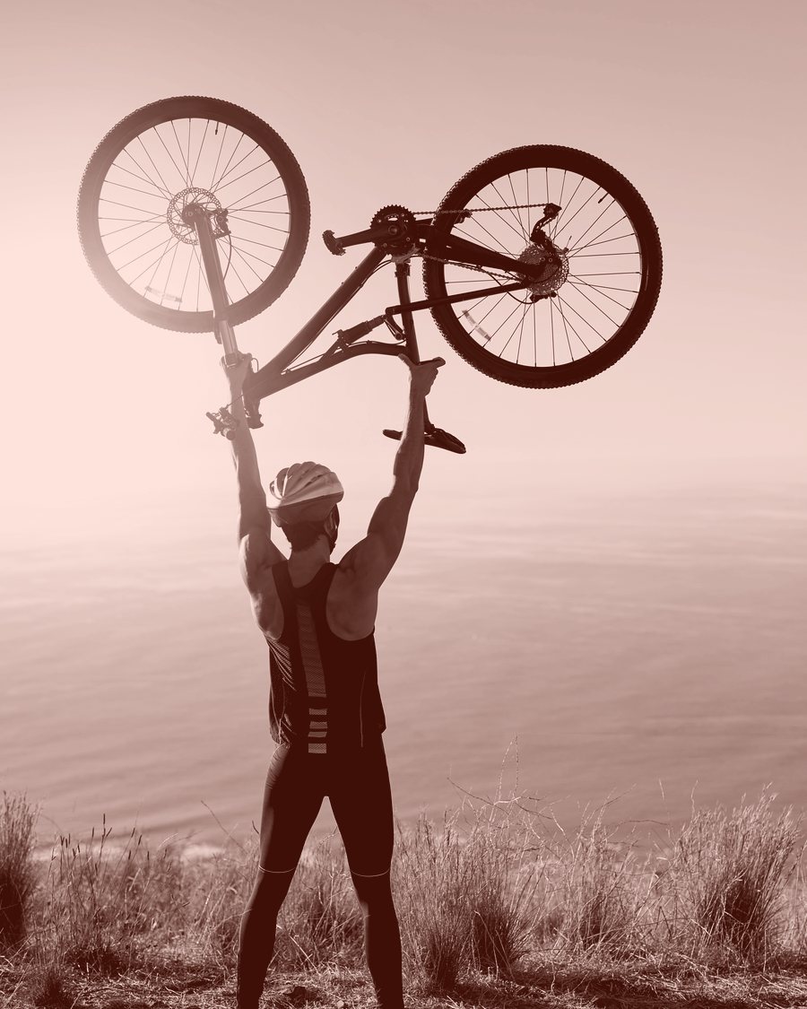 Wielrenner heft zijn fiets boven het hoofd op een heuveltop bij zonsopgang